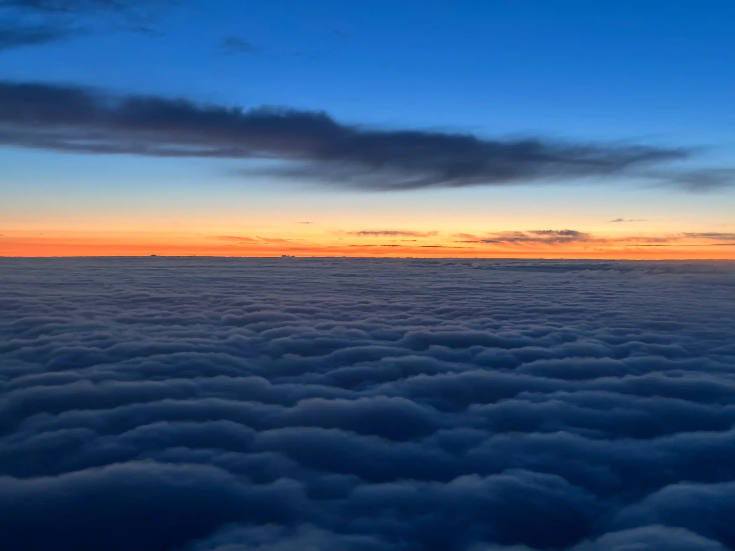 Breathtaking sunset over a sea of clouds with vibrant orange and deep blue sky creating a mesmerizing view above the horizon.