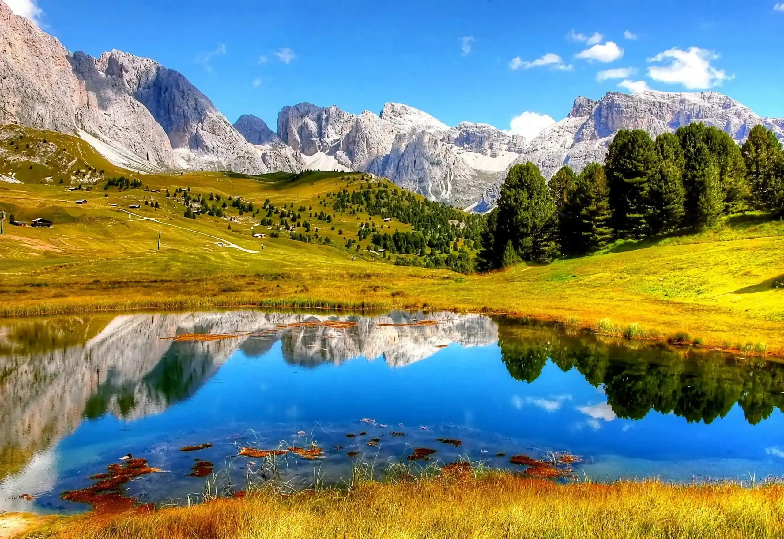 Scenic mountain landscape with a crystal-clear lake showing a stunning reflection of mountains on a clear alpine lake, with snowy peaks and green meadows.